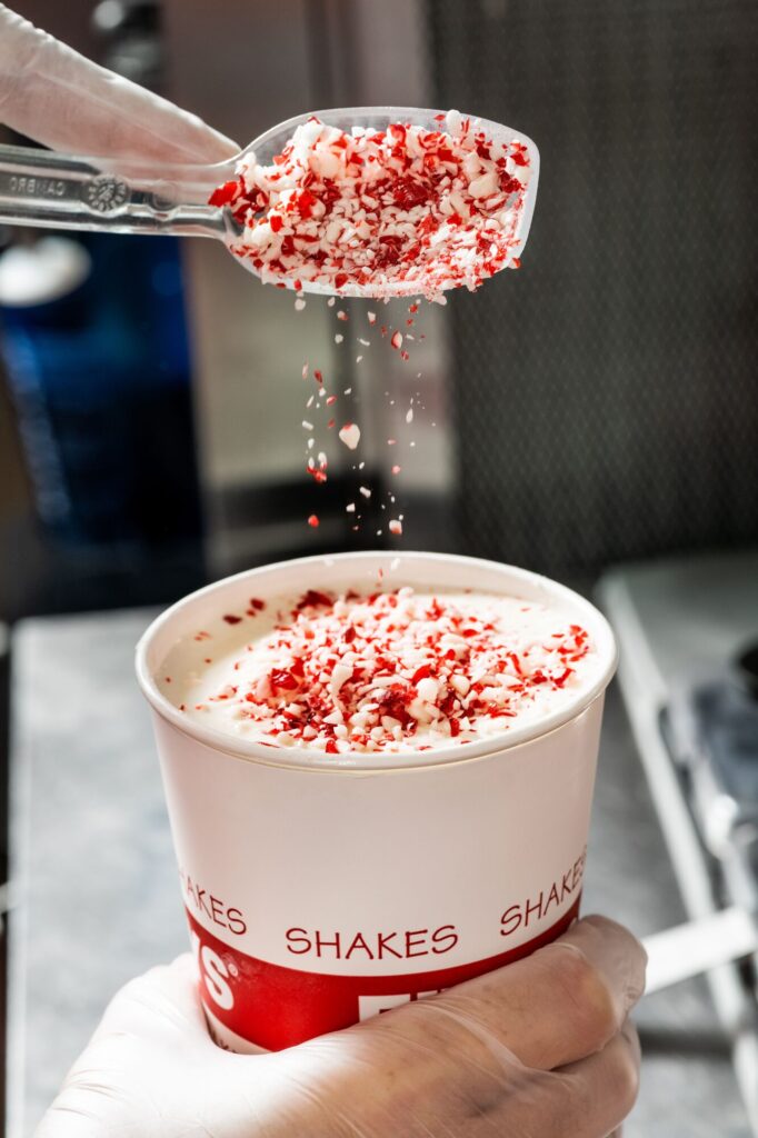 Scoop of Candy Cane Crunch being poured into a Five Guys milkshake.